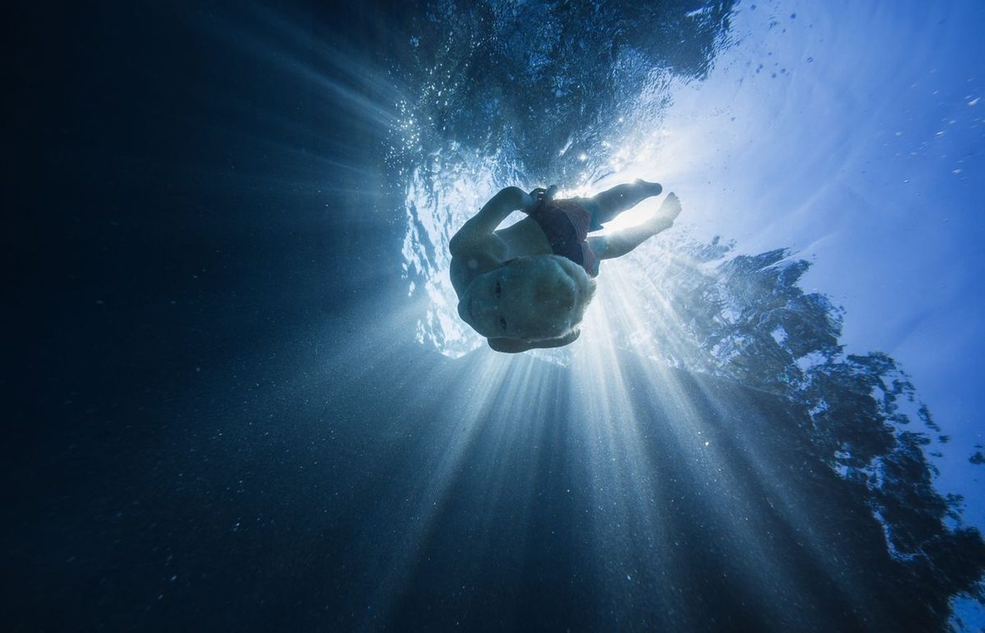 Chico nadando bajo el agua con los rayos de luz atravesando la superficie