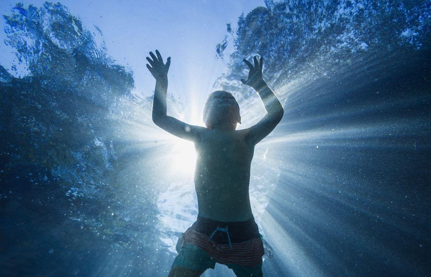Chico jugando bajo el agua con la luz del sol de fondo